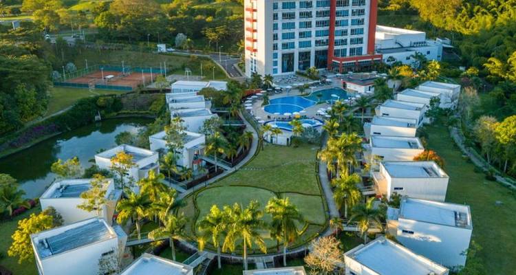 Luftaufnahme eines Resorts mit einem Pool und mehreren Gebäuden umgeben von Grünflächen.