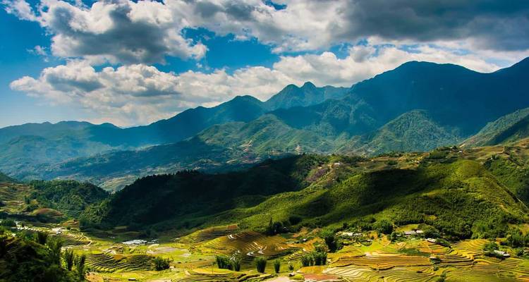 Campos en terrazas y montañas bajo un cielo nublado.