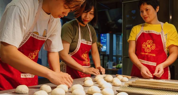 People wearing aprons making dough balls in a kitchen.
