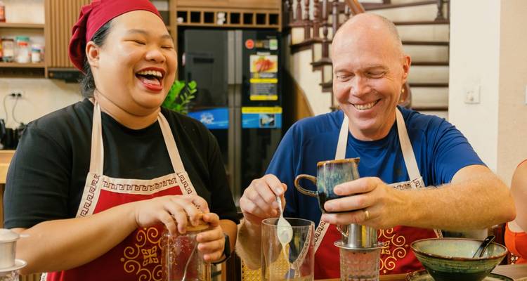 Two people laughing and preparing drinks in a kitchen.