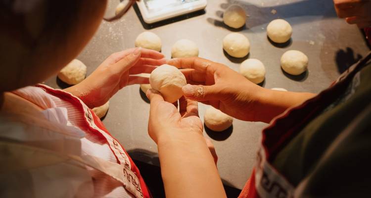 Hands shaping dough with more dough balls on the table.