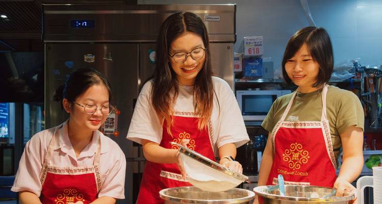 Three people wearing aprons baking in a kitchen.