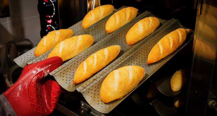 Freshly baked baguettes being taken out of an oven.