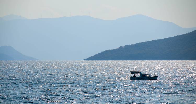 Un bateau de pêche solitaire sur une mer scintillante avec des montagnes au loin.