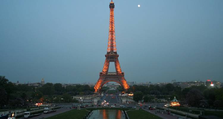 La Torre Eiffel iluminada al atardecer con la luna visible.