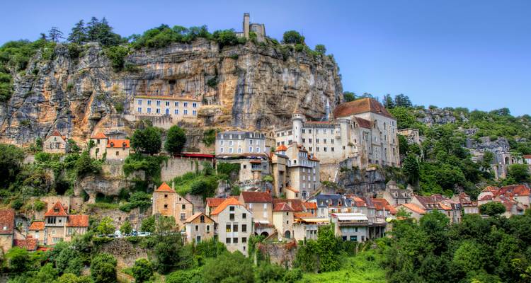 Pueblo medieval en acantilado con vegetación exuberante.