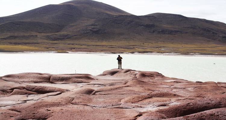 Een enkele persoon die bij een meer staat met heuvels op de achtergrond.