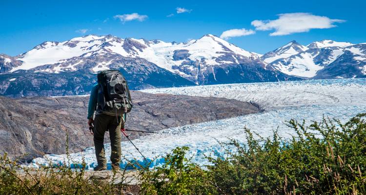 Persoon met een rugzak die naar een gletsjer en bergen kijkt.