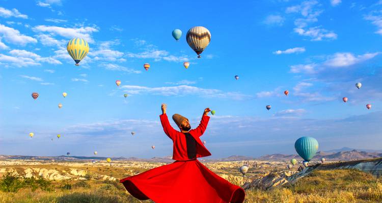 Hombre con vestimenta tradicional con globos aerostáticos en el fondo.