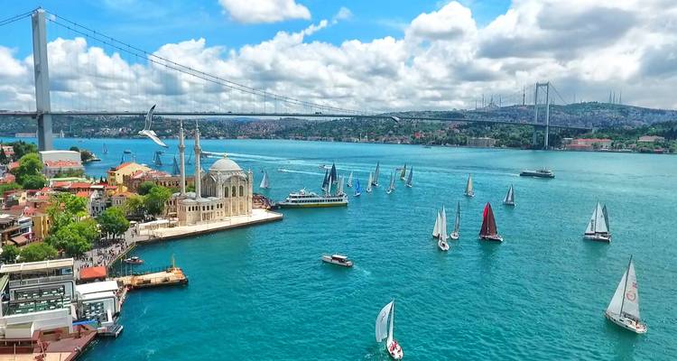 Veleros en un río con una mezquita y un puente al fondo.