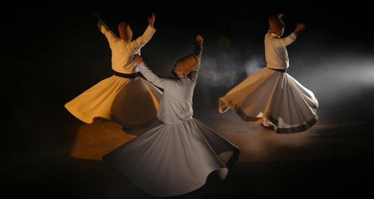 Bailarines con atuendo tradicional blanco girando en el escenario.