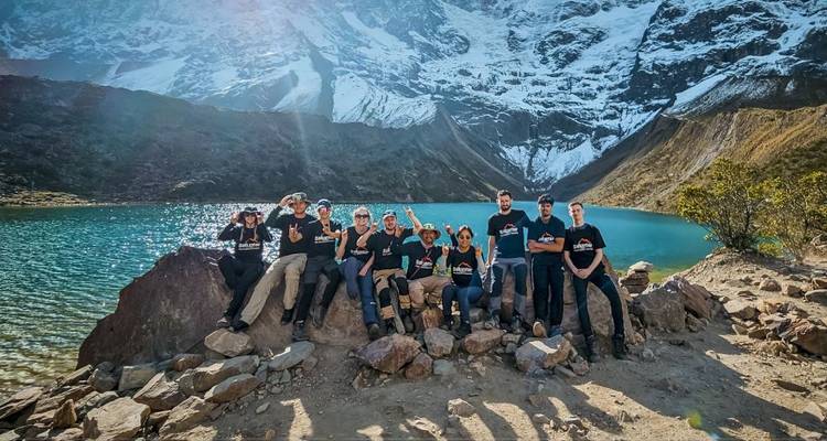 Grupo de personas junto a un lago cerca de montañas nevadas.