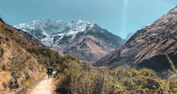 Personas caminando por un sendero con una montaña nevada de fondo.