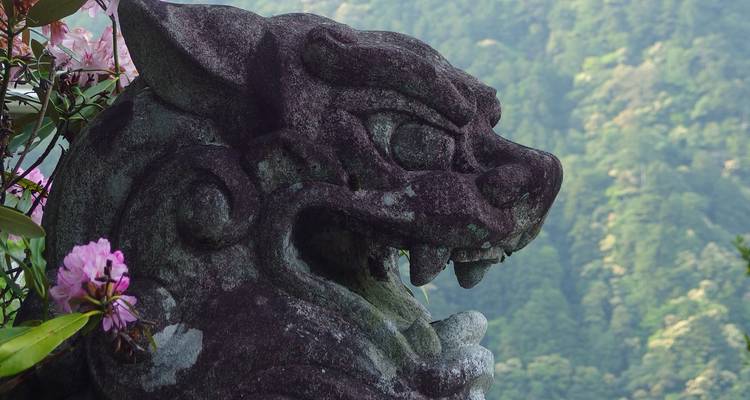 Estatua de piedra de una criatura mítica rodeada de follaje.