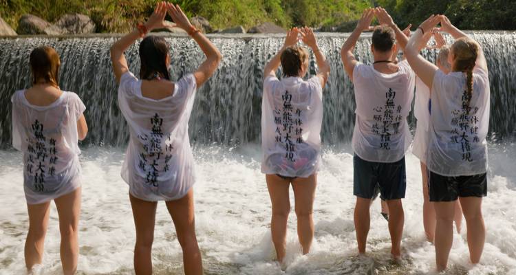 Grupo de personas de pie en un río con las manos levantadas.