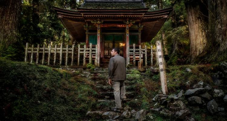 Hombre de pie frente a un pequeño santuario japonés tradicional.