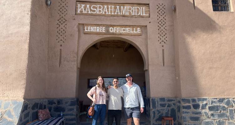 Tres personas de pie frente a una kasbah histórica.