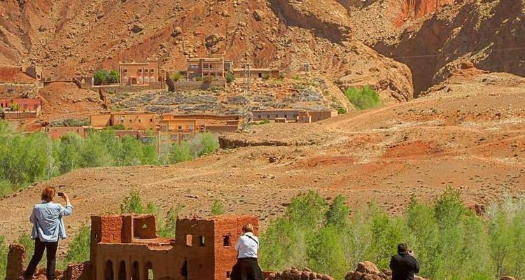 Turistas fotografiando una vista panorámica de montañas desérticas con ruinas en primer plano.