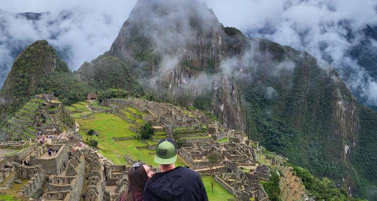 Pareja admirando las ruinas de Machu Picchu con montañas cubiertas de niebla.