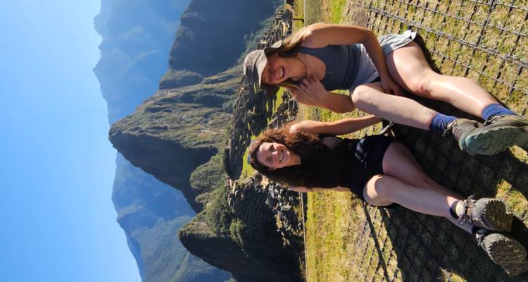 Dos mujeres sentadas frente a las icónicas montañas de Machu Picchu.