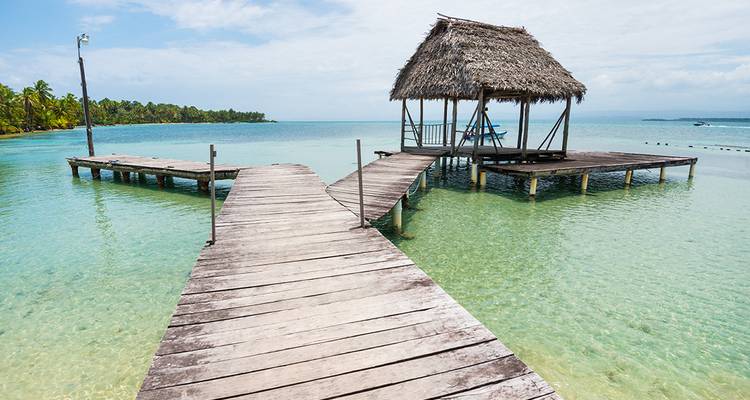 Vredige strandscène met een rieten hut boven helder turquoise water.