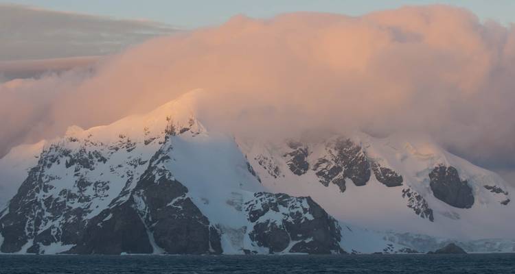 Besneeuwde bergen met dramatische wolken bij zonsondergang