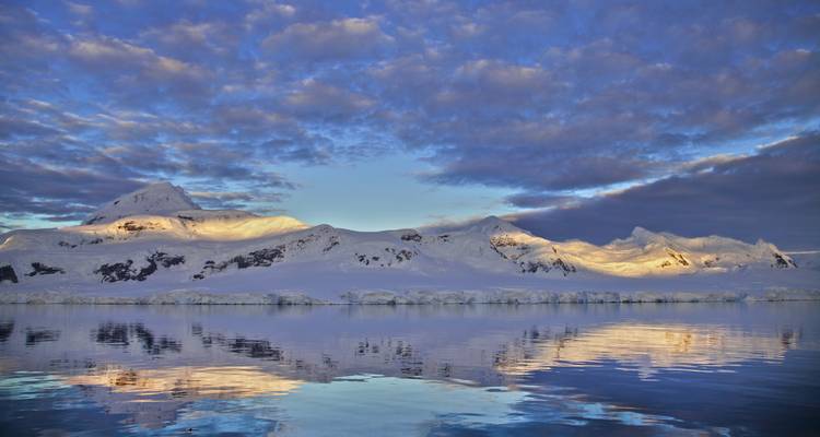 Snow-covered mountains and reflection on calm water.