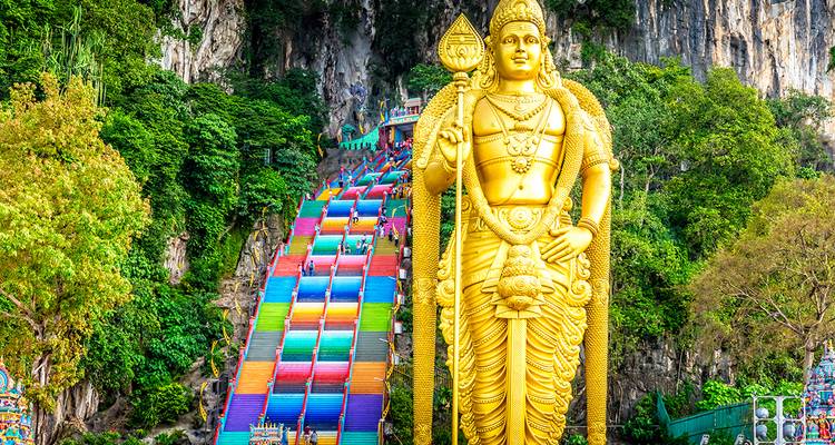 Touristes grimpant les marches colorées menant aux grottes de Batu avec une statue dorée au premier plan.