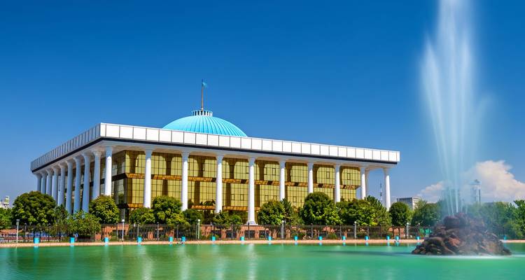 Tashkent’s modern parliament building framed by a powerful fountain plume under cloudless skies.