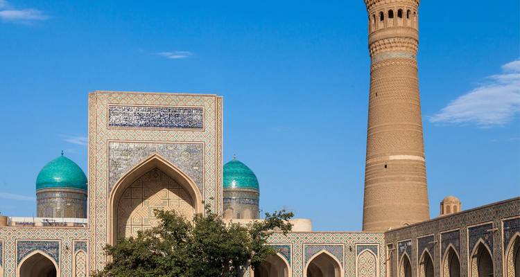 The towering Kalyan Minaret rises beside turquoise-domed madrasa against a crisp blue sky.