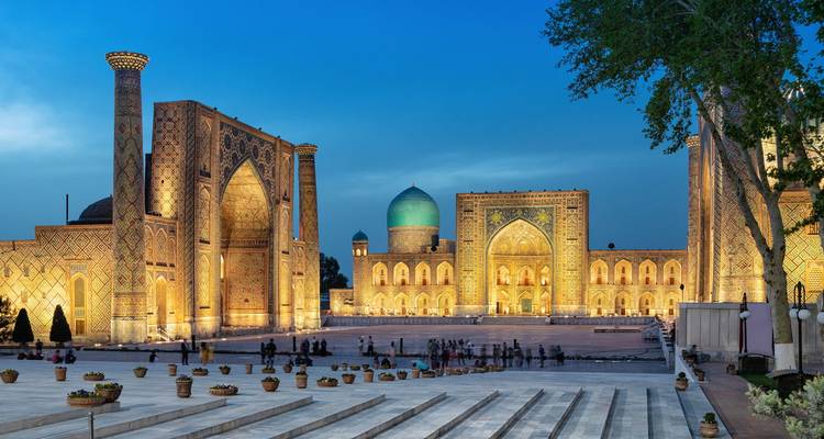 L'ensemble illuminé du Régistan brille au crépuscule, ses majestueuses madrasas entourant une vaste place avec des visiteurs.