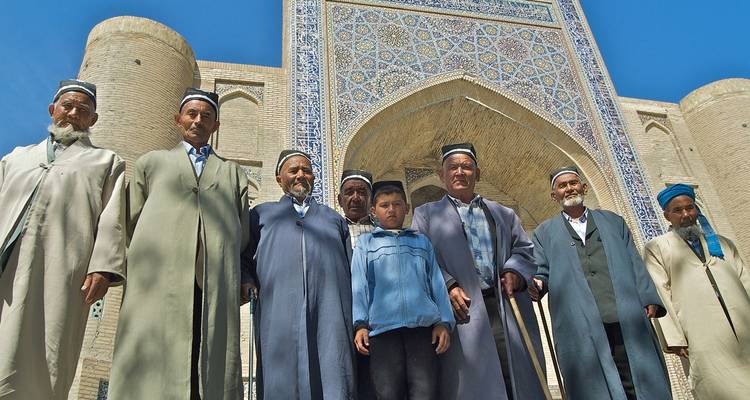 Des hommes locaux et un garçon posent fièrement dans des chapeaux traditionnels devant un portail richement carrelé sous un ciel bleu éclatant.