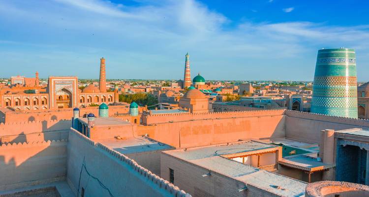 Panorama baigné de soleil des murs en terre crue de Khiva, des dômes turquoise et du trapu Kalta Minor disposés parmi les teintes désertiques.