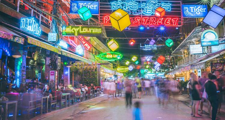 Rue animée avec des enseignes au néon et des gens au Cambodge.