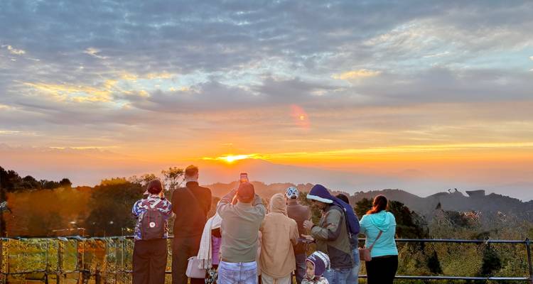 Reisegruppe betrachtet einen Sonnenuntergang über hügeliger Landschaft.