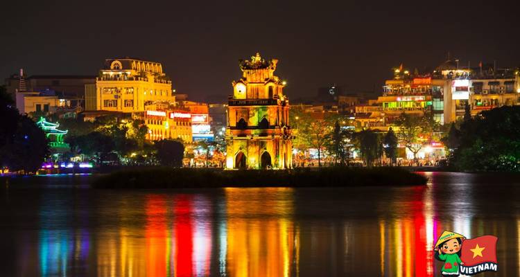 Nachtbeeld van een toren en stadslichten weerspiegeld op het water.