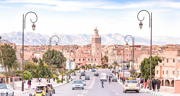 Breite Stadtstraße, die zu einem Turm mit Bergkulisse führt.