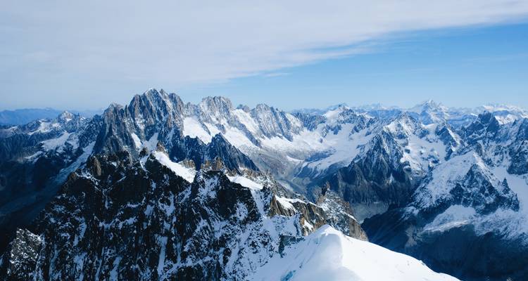 Panorama en haute altitude de pics déchiquetés couverts de neige s'étendant à travers le massif du Mont Blanc sous un ciel bleu pâle.