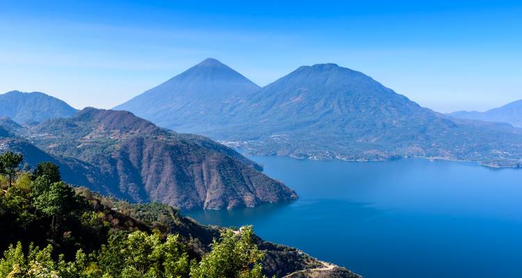 Luftaufnahme eines tiefblauen Sees, umgeben von Vulkanbergen und Grün.