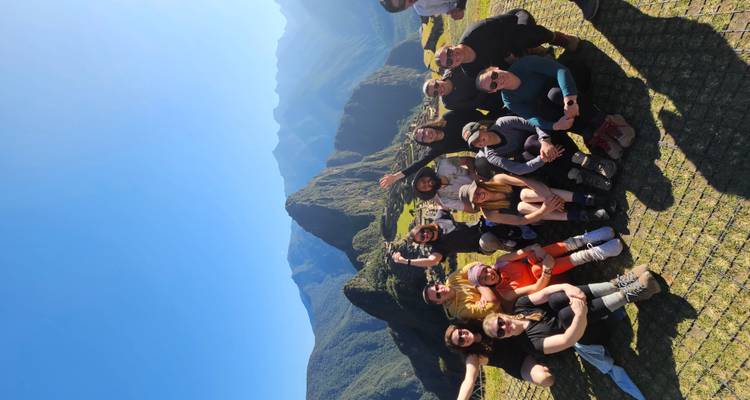 Grupo de personas posando en Machu Picchu con montañas de fondo.