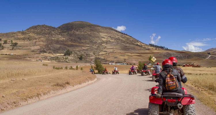 Personas montando cuatrimotos en un camino de tierra con montañas.