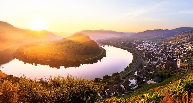 Malerische Flussbiegung mit einem Dorf bei Sonnenaufgang.