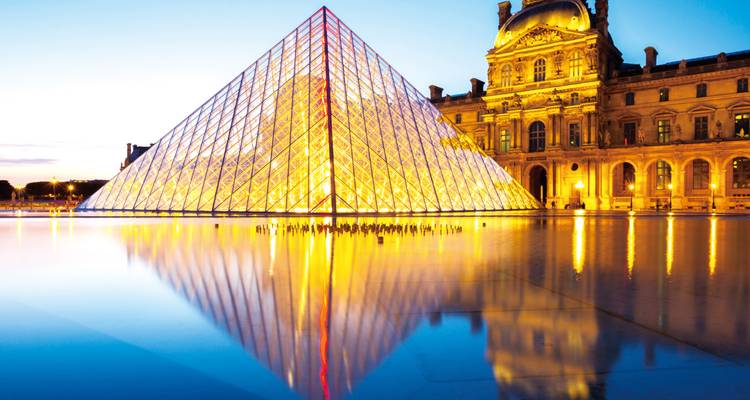 Pyramide du Louvre illuminée et palais reflétés dans l'eau calme au crépuscule.