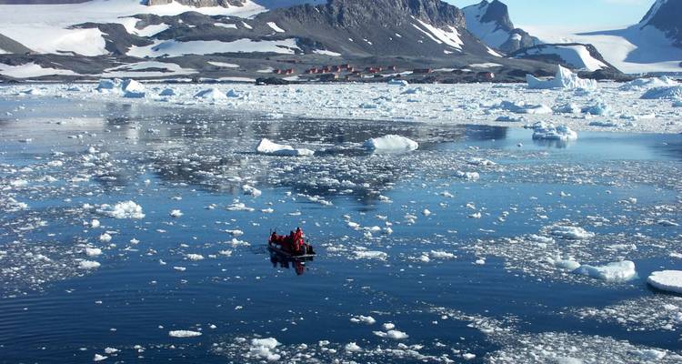 Touristes dans un bateau entouré d'icebergs et d'une station lointaine.