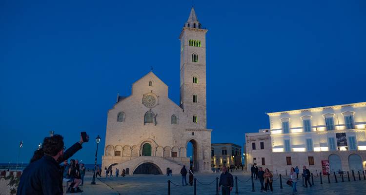 Vue à l'heure bleue de la Cathédrale de Trani illuminée tandis que les visiteurs prennent des photos sur la place.