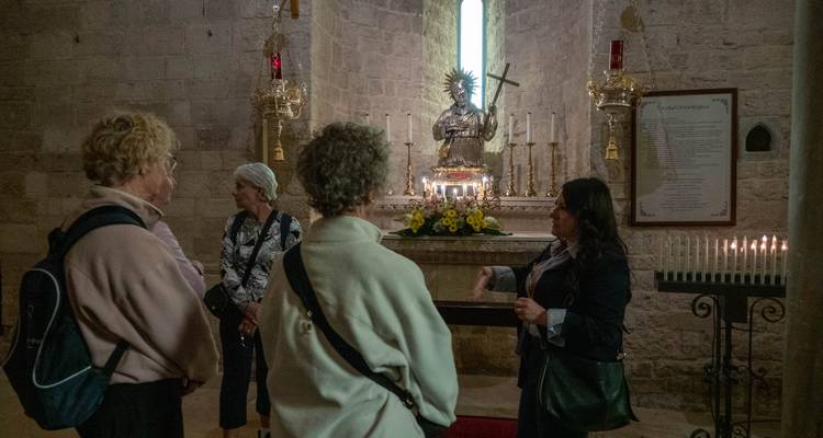 Intérieur de chapelle faiblement éclairé où un guide explique un autel doré à des visiteurs attentifs.