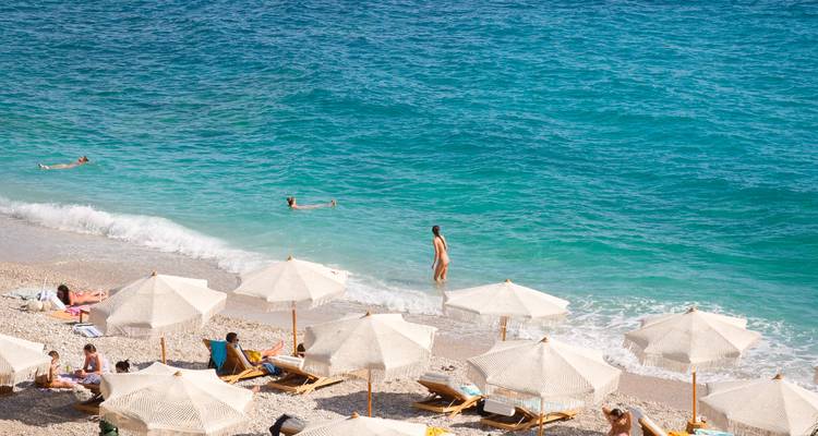 Plage avec des parasols et des gens qui nagent dans la mer.