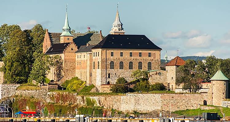 La Fortaleza de Akershus en Oslo iluminada por una cálida luz, con dos torres puntiagudas elevándose sobre muros de piedra.