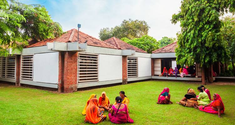 Mujeres con vestimenta colorida sentadas en el césped de un edificio moderno.