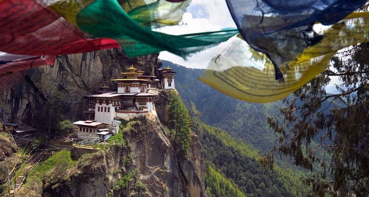 Bhutanisches Kloster am Klippenrand mit bunten Gebetsfahnen, die im Wind flattern.